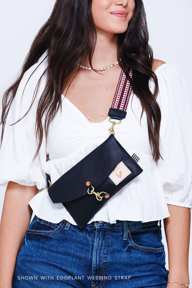 Woman wearing a small black leather envelope clutch and crossbody with a red/pink webbing crossbody strap attached to it