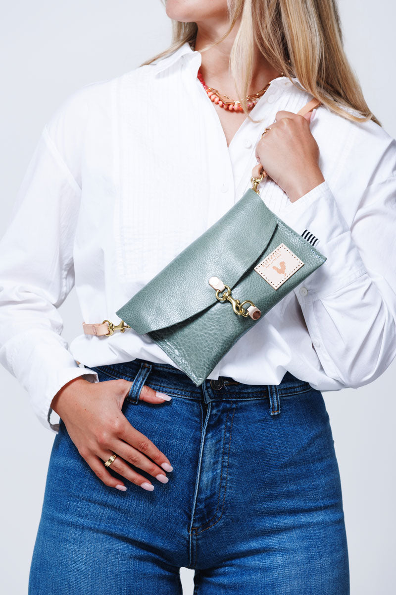 Model displaying a sea foam green small clutch with a cream colored strap as a cross body bag