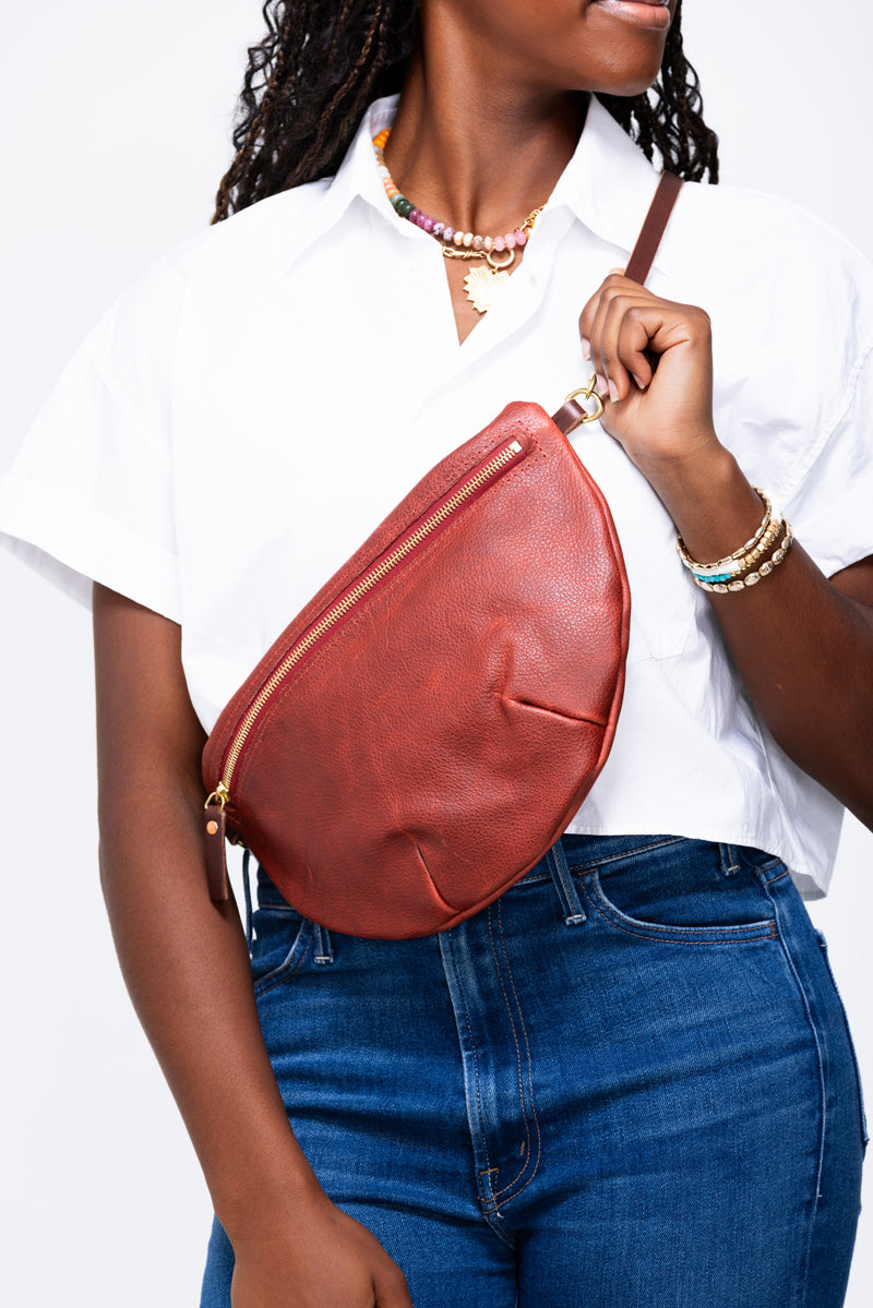 Model wearing a reddish tan leather fanny pack bag as a cross body bag.