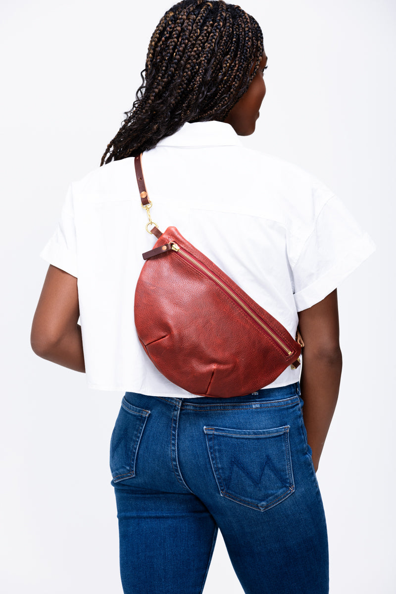 Model wearing a fanny pack reddish tan leather bag as a crossbody bag on her back.