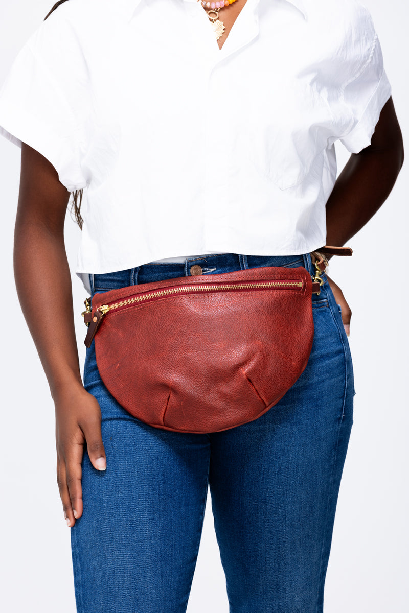 Model wearing a reddish tan leather fanny pack with a zippered opening