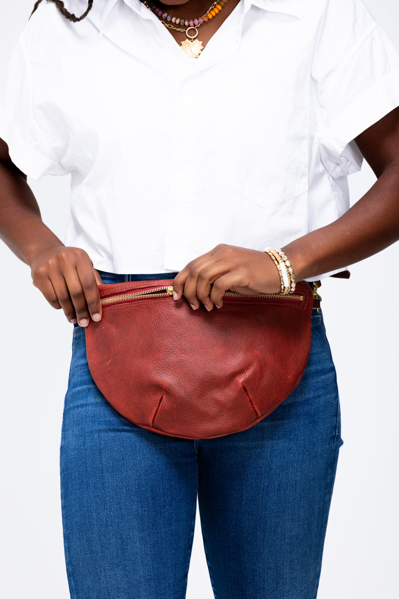 Model zipping closed a reddish tan leather fanny pack bag.