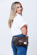 Model looking over her shoulder while displaying a medium sized dark brown leather purse with waist length shoulder straps and front clasp