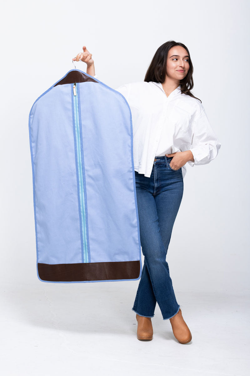 Picture of model holding out a blue garment bag with dark brown leather trim.