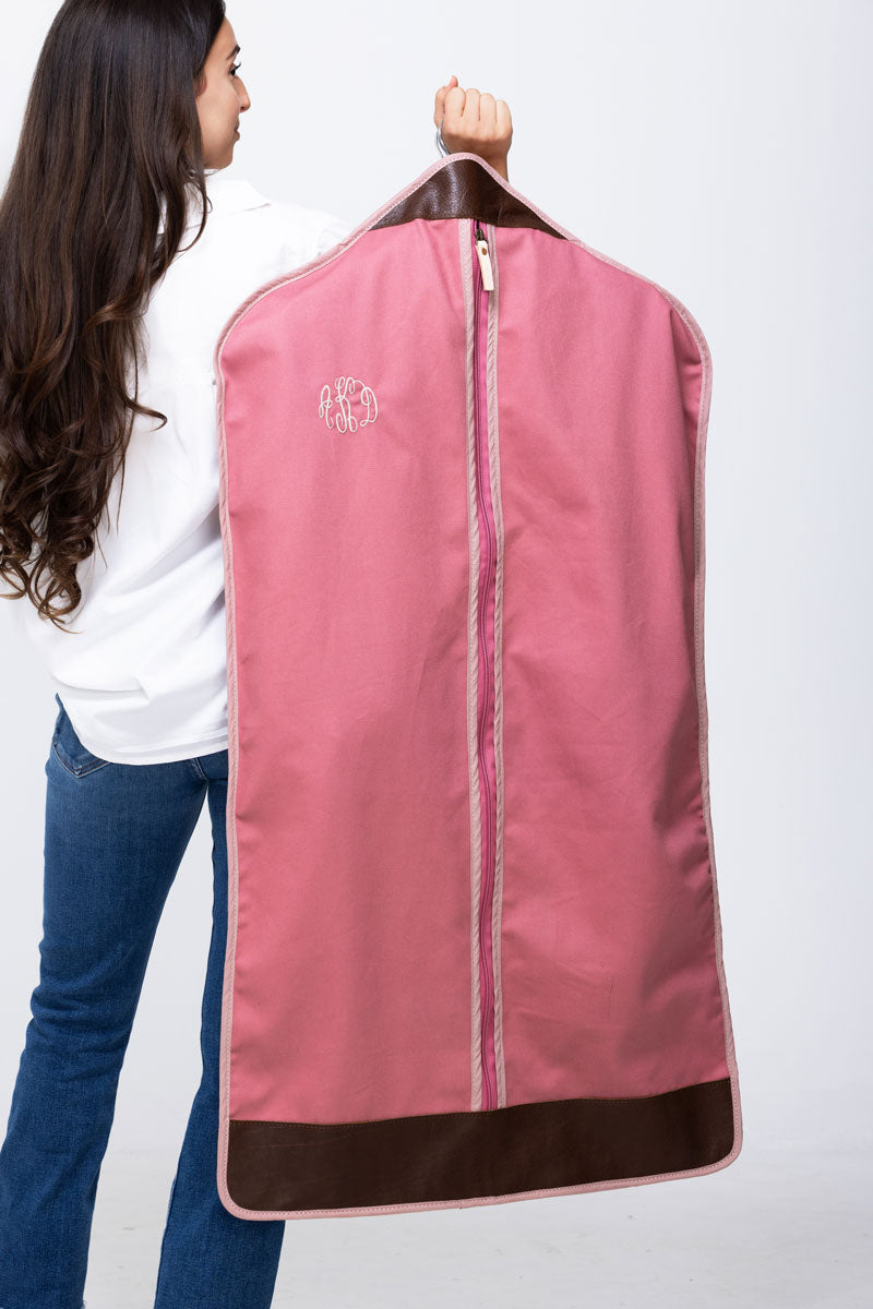 Picture of model holding a monogrammed pink garment bag with dark brown leather trim over her shoulder.