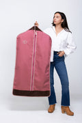 Picture of model holding a monogrammed pink garment bag with dark leather trim.