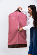 Picture of model zipping closed a monogrammed pink garment bag with dark brown leather trim.