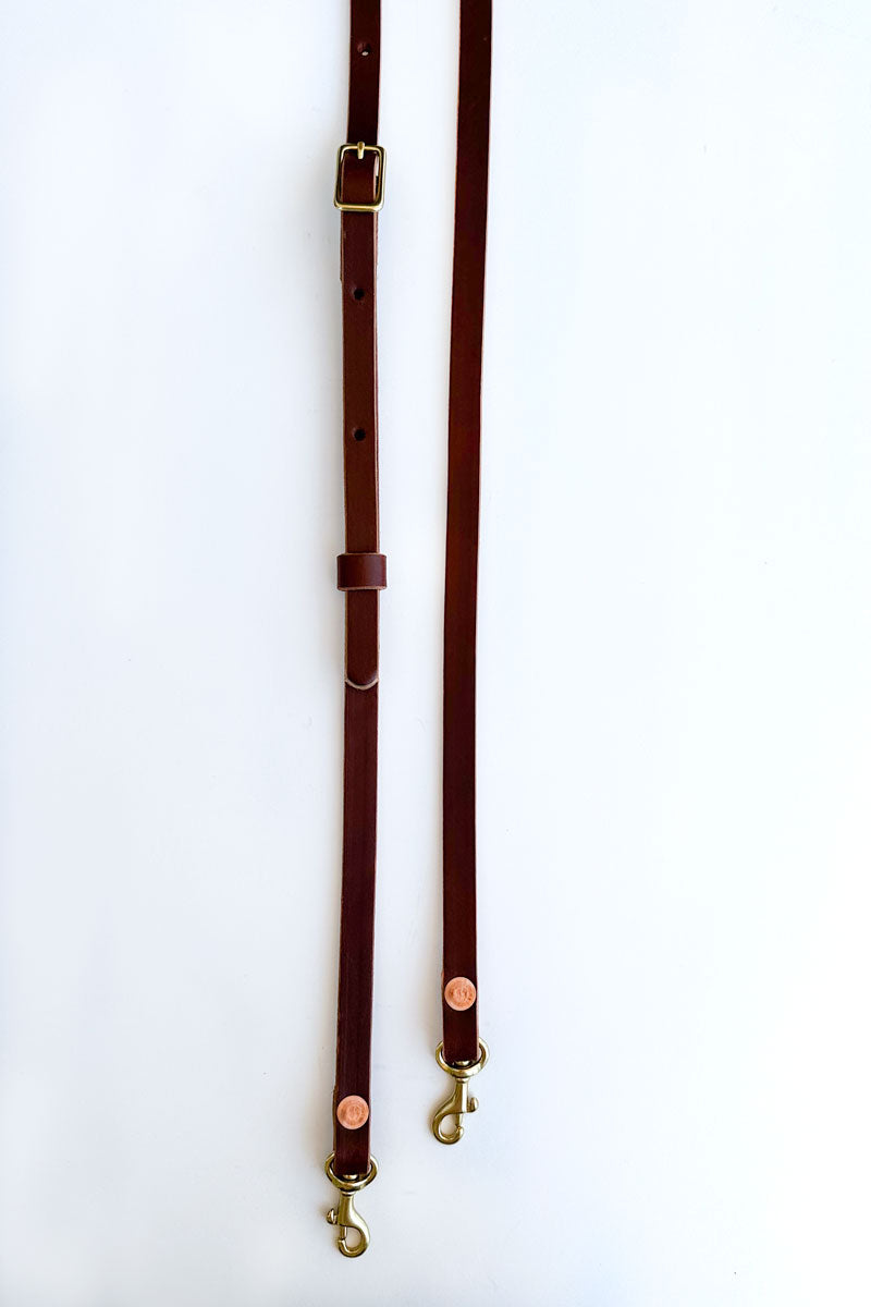 Two adjustable leather brown crossbody/shoulder straps next to each other (one longer, one shorter)