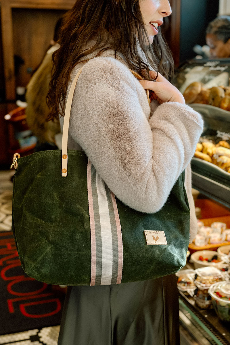 Model displaying brushed leather olive green tote with cream and grey accent stripes down the center and cream colored shoulder straps.