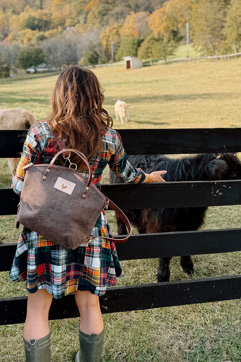 Woman in dress reaching to pet a cow. She is wearing a brown mottled leather bag with brown leather straps.