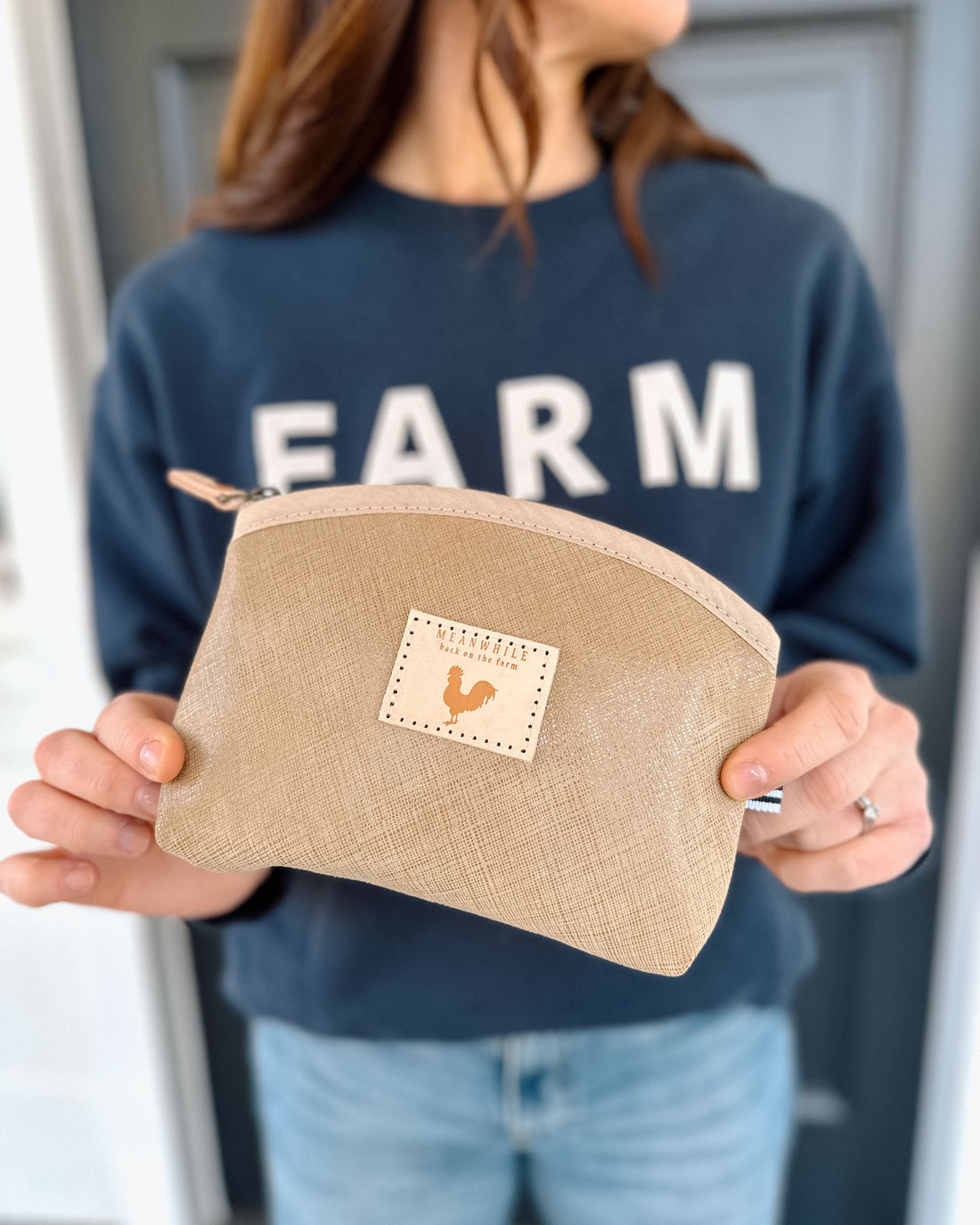 Picture of model in navy blue sweatshirt holding out a cream colored, leather zippered pouch.