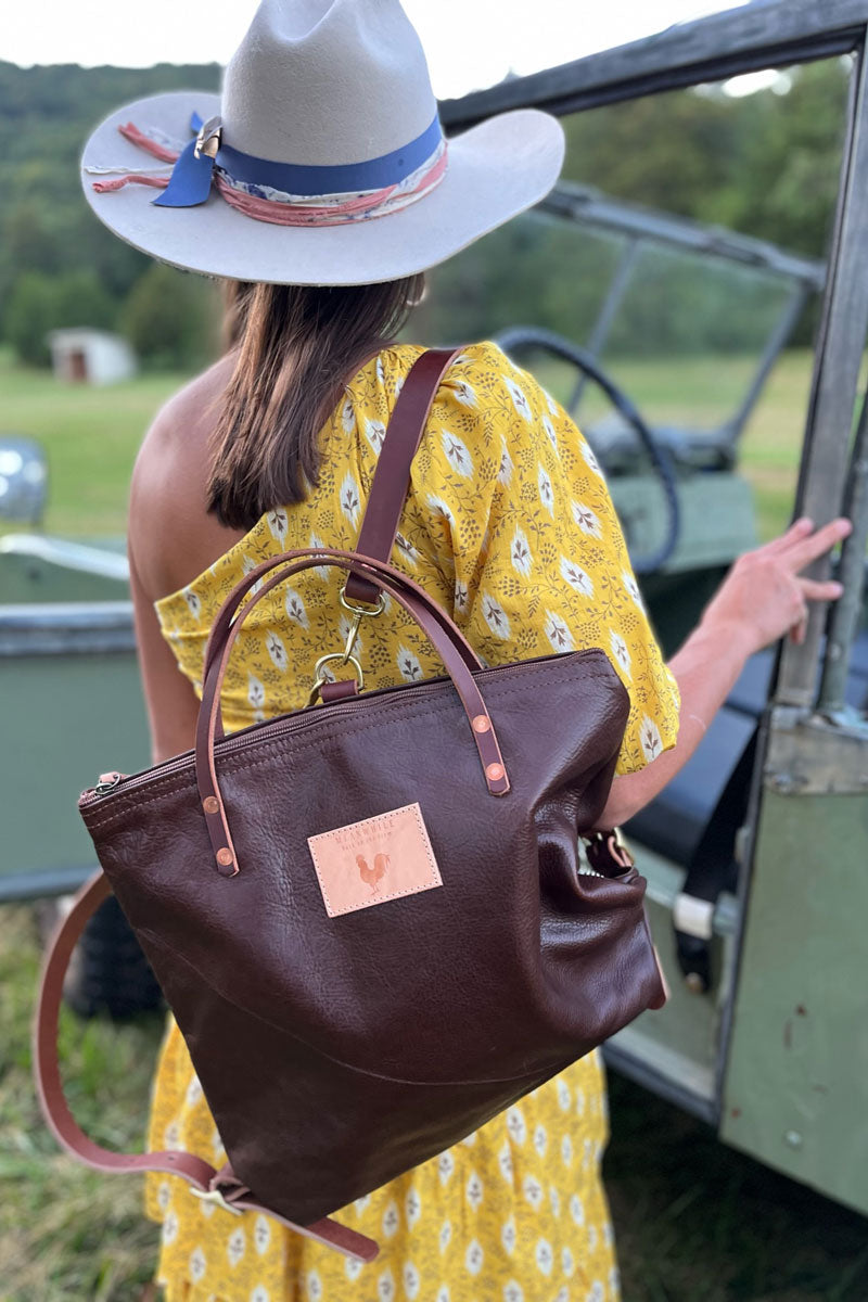 Model wearing large dark brown leather bag with brown shoulder strap