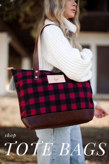 Model in chunky knit white sweater wearing red and black checked tote with dark brown leather straps and bottom. Text on photo reads "shop TOTE BAGS"