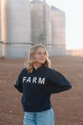 Model standing in front of silos wearing a dark blue sweatshirt with the word 