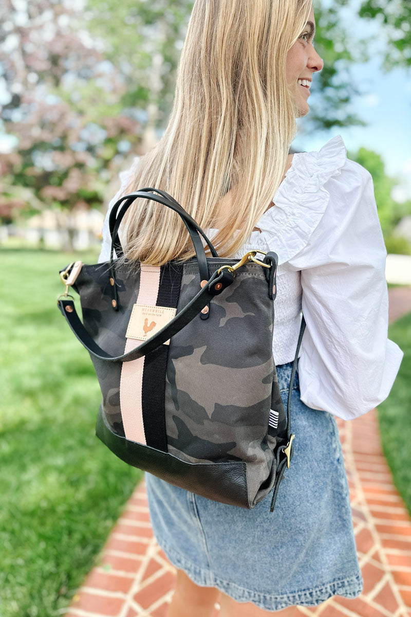 Girl walking on a brick sidewalk wearing a black camo leather convertible backpack with a black/cream stripe on her back