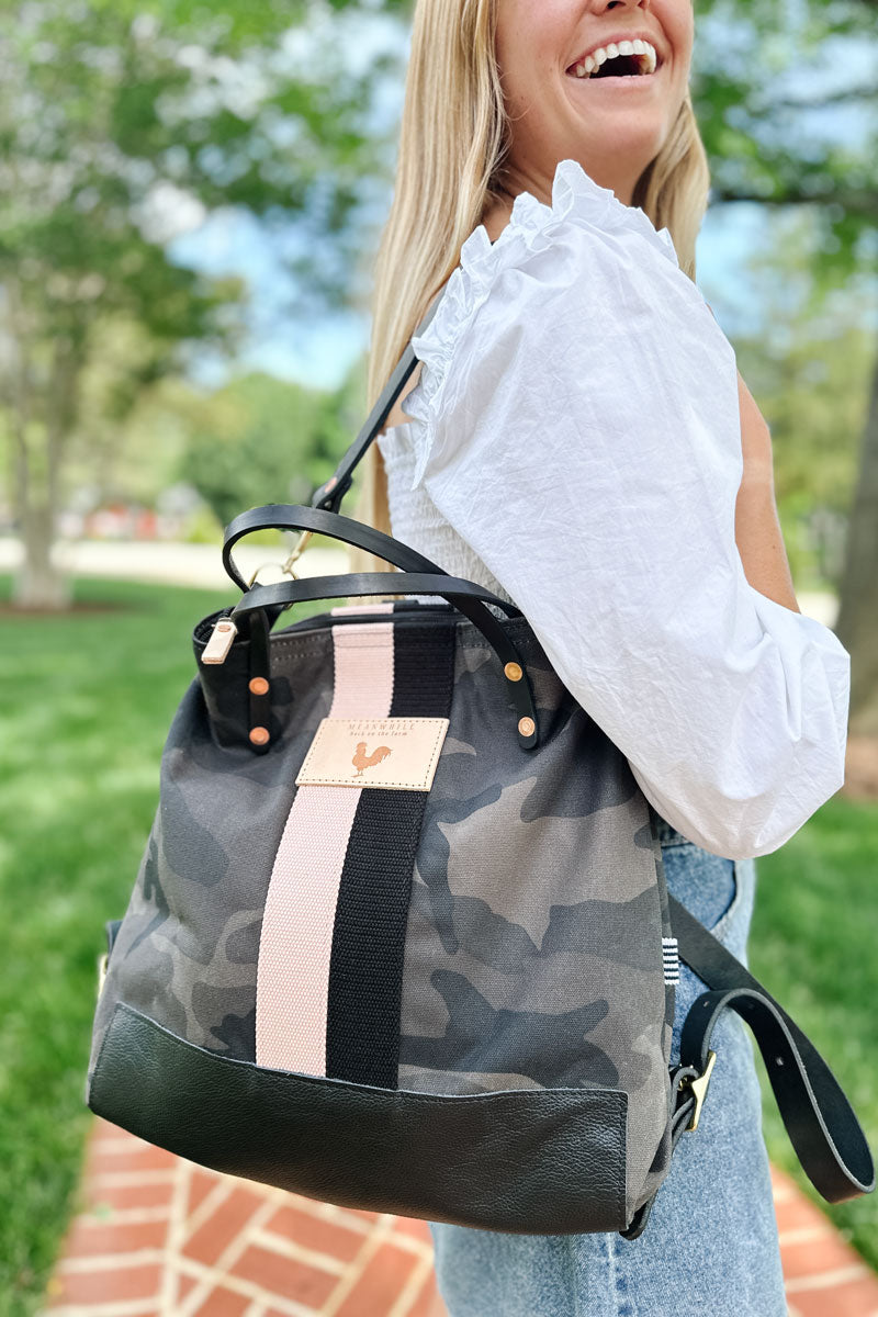 Girl walking on a brick sidewalk wearing a black camo leather convertible backpack with a black/cream stripe on her back