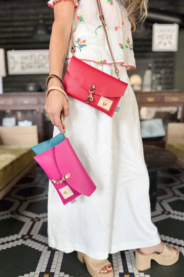 Model holding several leather wristlet clutch bags with option shoulder strap. Bags are in bright pink, teal and orange.