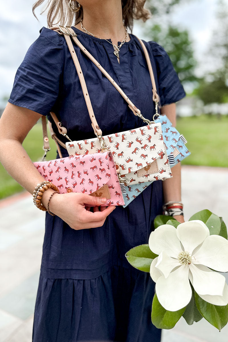 Girl wearing three envelope clutch/purses on her shoulder with small brown horses pattern on each one (bright pink, white, and light blue)