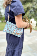 Girl wearing a light blue envelope clutch/purse on her shoulder with small brown horses pattern