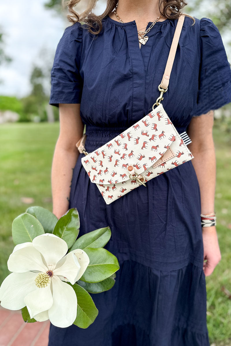 Girl wearing a white envelope clutch/purse across her chest with small brown horses pattern