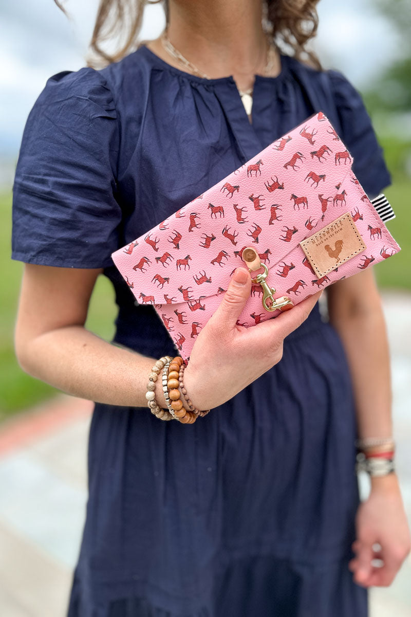 Girl holding a bright pink leather envelope clutch with small brown horses pattern