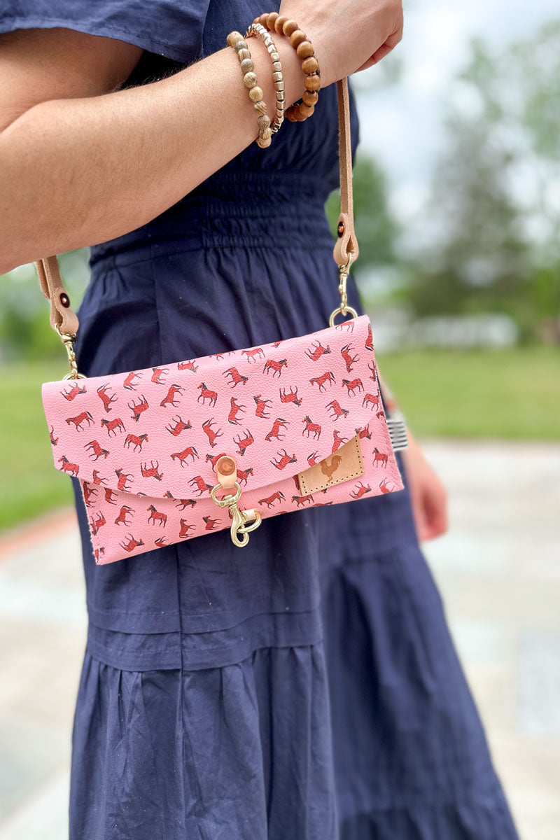 Girl wearing a bright pink leather envelope clutch purse with small brown horses pattern on her shoulder