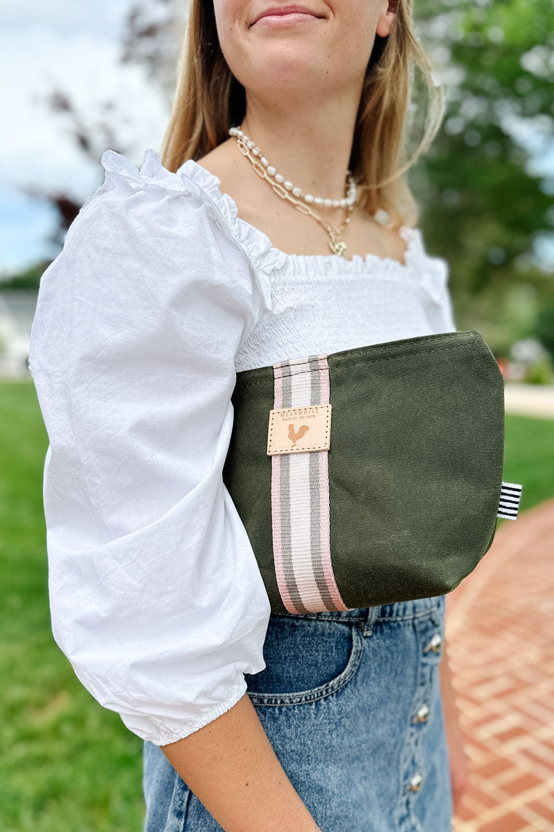 Girl holding a small olive green leather makeup bag with a white/gray stripe under her arm