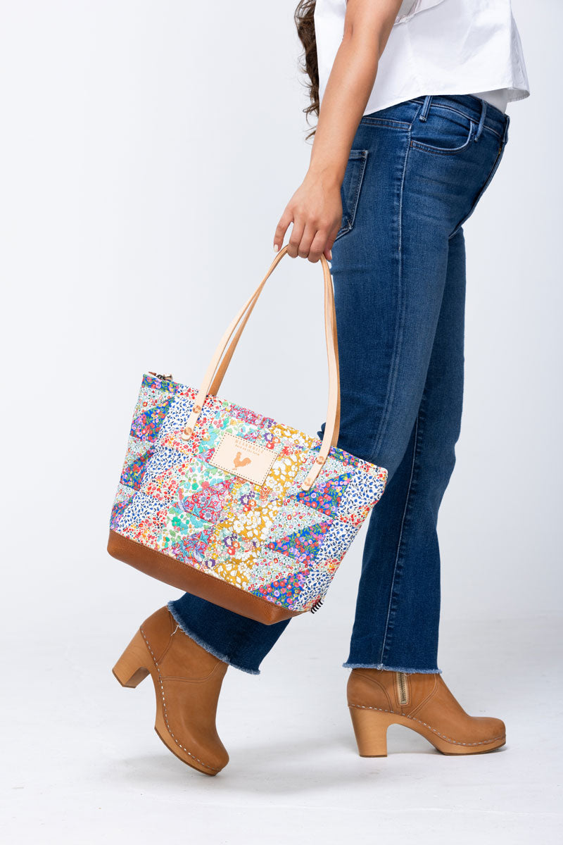 Model swinging large quilted floral bag with cream colored handles and tan leather bottom.