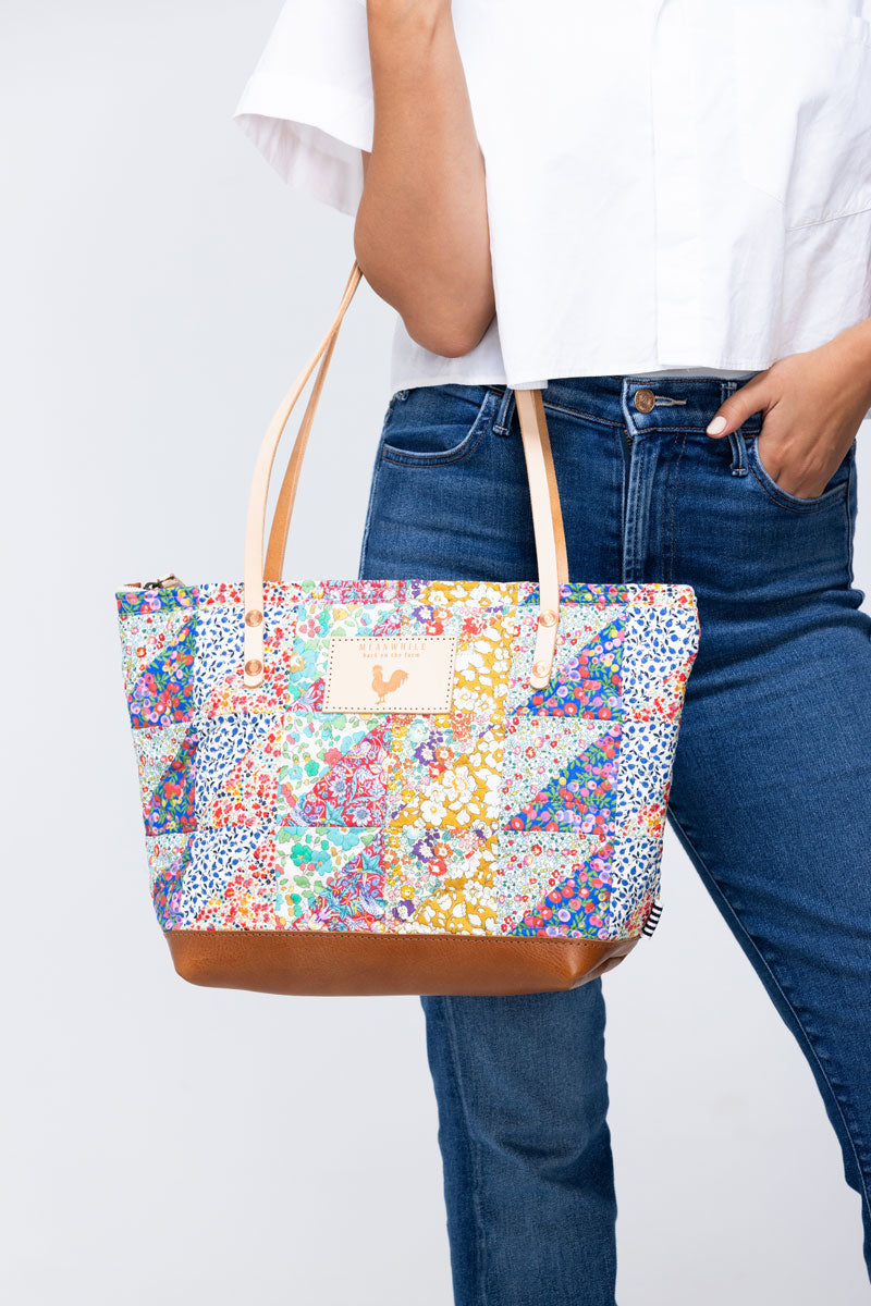 Model holding floral quilted bag with tan handles and leather bottom