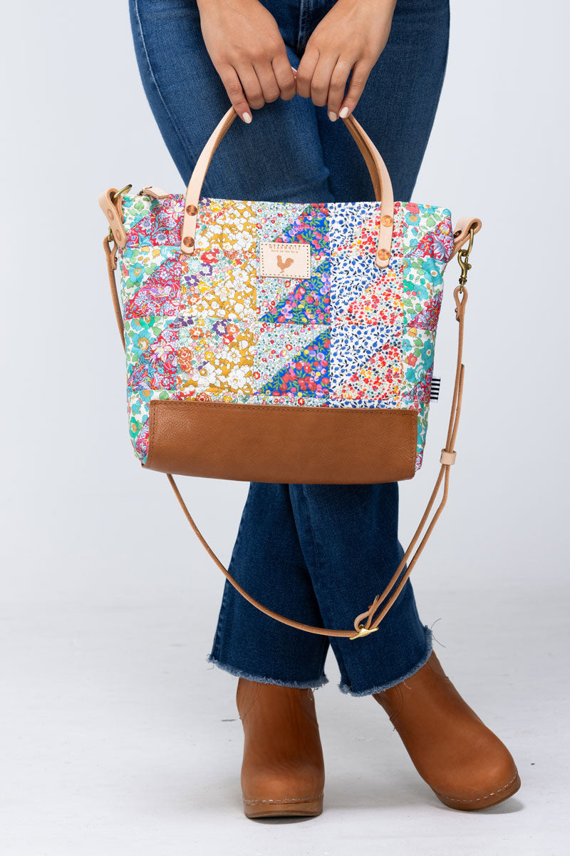 Model holding large floral quilted hand bag with tan leather straps and bottom