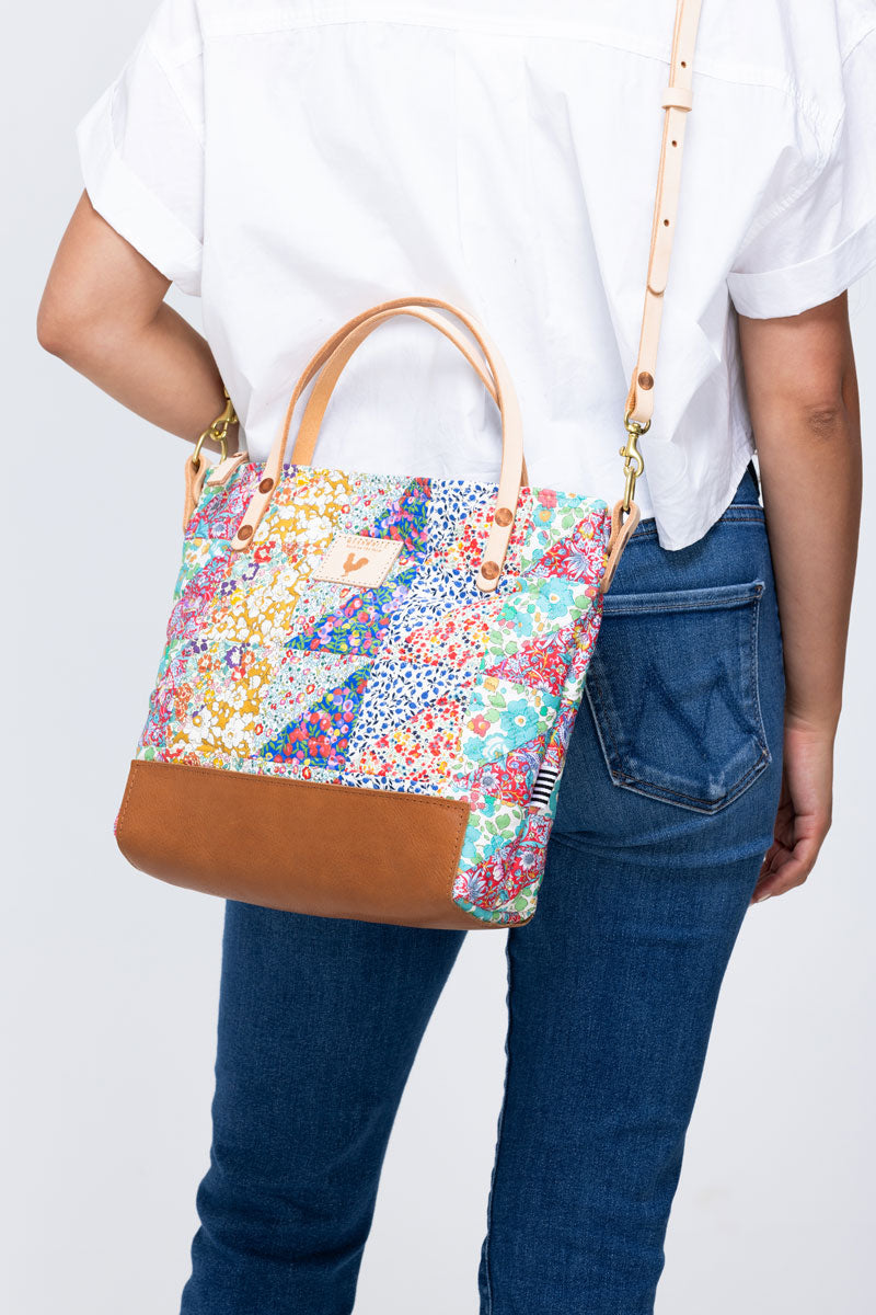 Rearview of model wearing a quilted floral print handbag with cream colored straps and tan leather bottom