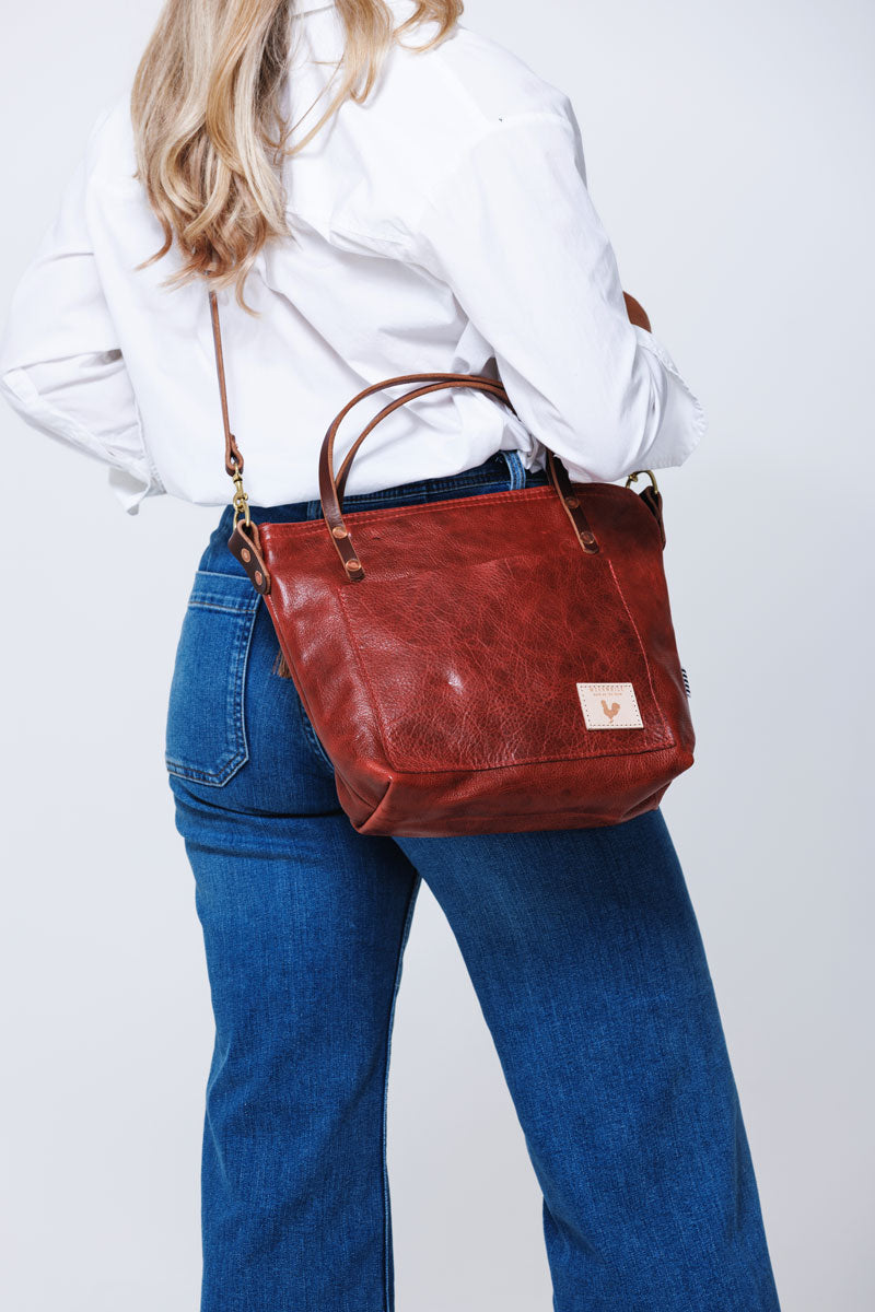 Model displaying a medium sized ruby leather bag. She is wearing the bag by a long shoulder strap