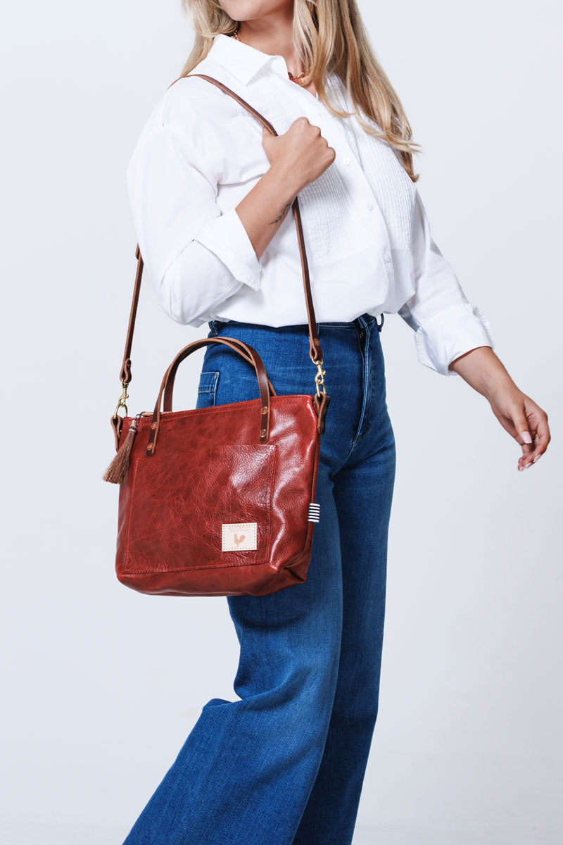 Model looking back over her shoulder and wearing a red leather bag with a shoulder strap and brown tassel