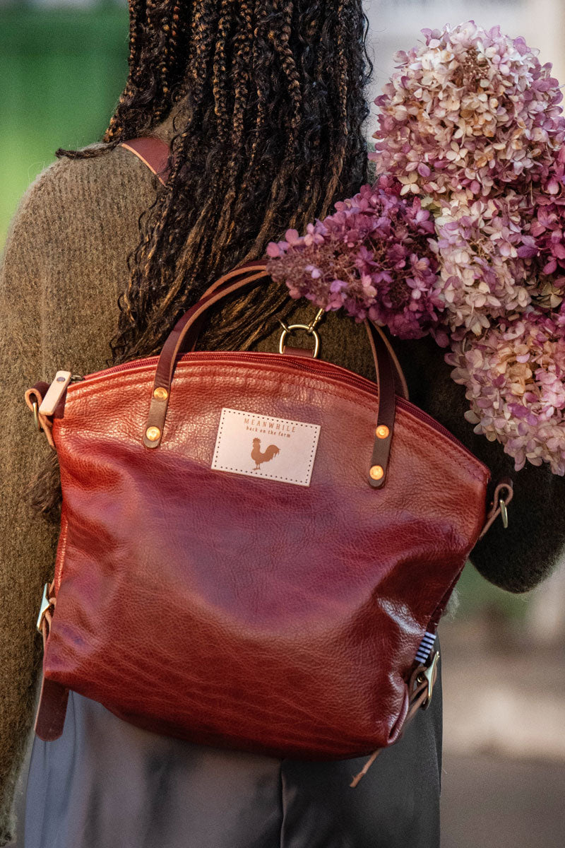 Model wearing red leather back pack style tote with blue and white ribbon tied to it.