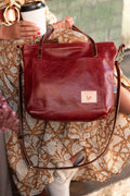 Woman wearing orange dress sitting down holding a white cup and a red/brown leather small tote in her hand