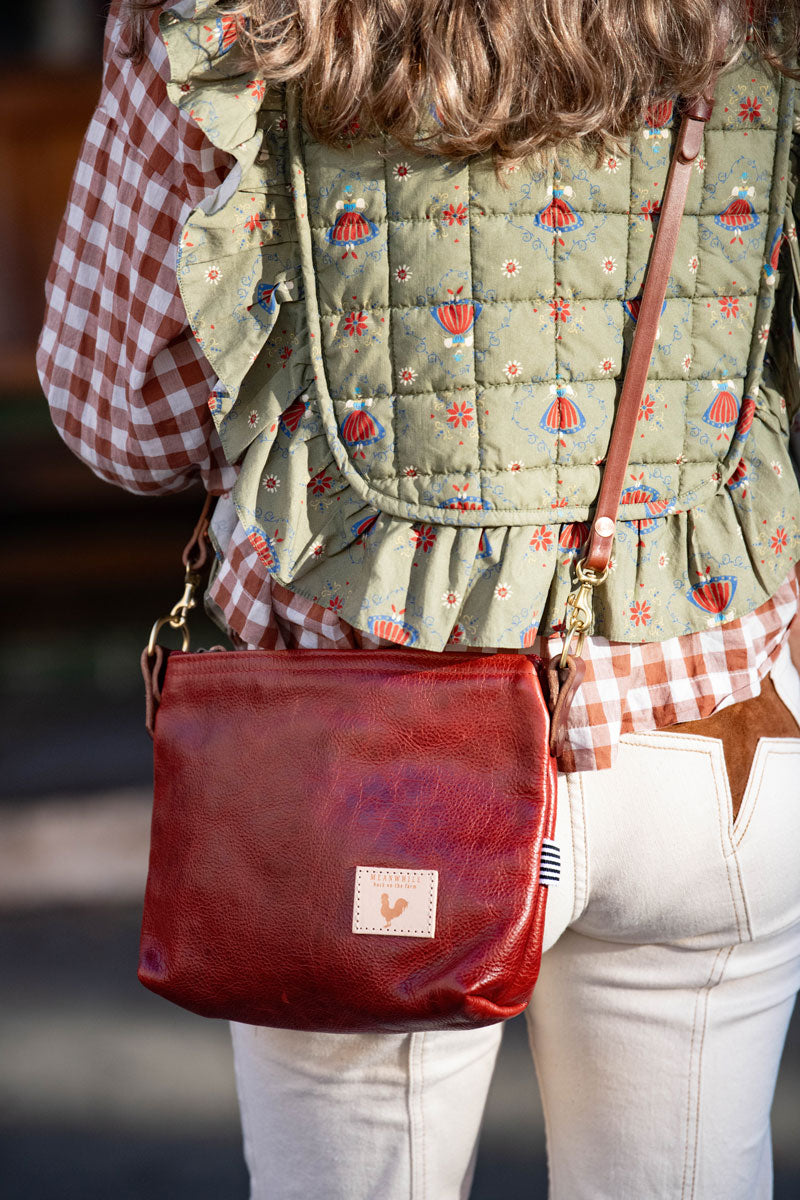 Model wearing ruby red leather bag with a long shoulder strap